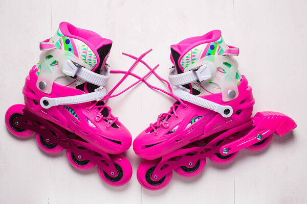 A pair of pink stylish roller skates on a white wooden background