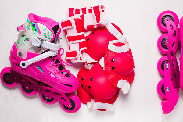 A pair of pink stylish roller skates on a white wooden background