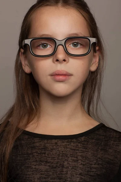 Retrato de uma menina de oito anos de idade com um humor calmo, em uma blusa preta e óculos com aro preto. Sessão de fotos estúdio — Fotografia de Stock