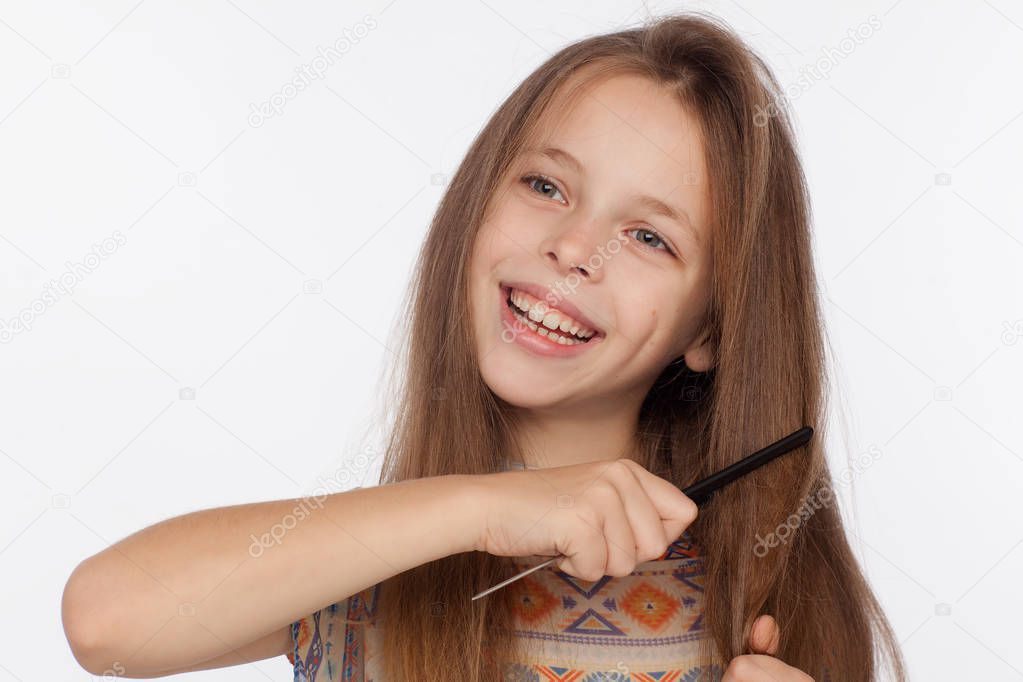 Portrait of an eight-year-old girl who is combing her hair with a comb. Studio photo shoot on a white background