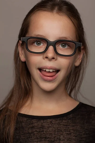 Retrato de uma menina de oito anos de idade com um humor calmo, em uma blusa preta e óculos com aro preto. Sessão de fotos estúdio — Fotografia de Stock