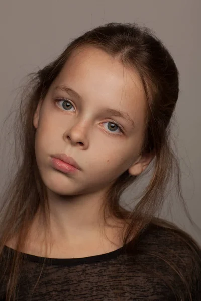Retrato de uma menina de oito anos de idade com um humor calmo, em uma blusa preta e com cabelo pego. Sessão de fotografia de estúdio. Fundo cinzento — Fotografia de Stock