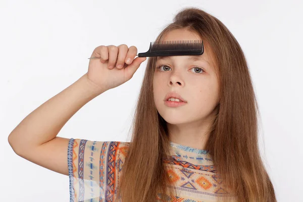 Retrato de uma menina de oito anos que penteia o cabelo com um pente. Estúdio sessão de fotos em um fundo branco — Fotografia de Stock