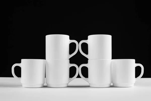 Arrangement of six white mugs with a handle. Black background