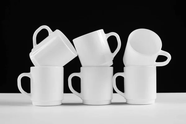 Arrangement of six white mugs with a handle. Black background