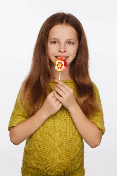 Emotionele portret van een achtjarig meisje in een geel-groene trui en met een lolly in haar handen — Stockfoto