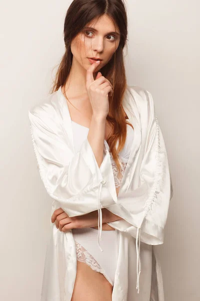 Sexy woman in white robe and white lingerie. Studio photo session