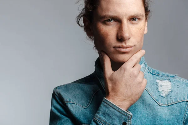 Portrait of a handsome long-haired man with drawn hair and freckles dressed in a denim shirt