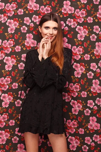 Retrato de una hermosa mujer vestida de negro. El fondo de la tela en el dibujo las flores — Foto de Stock