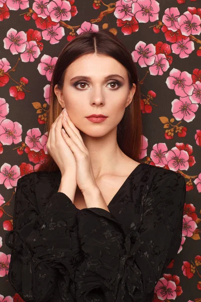 Retrato de una hermosa mujer vestida de negro. El fondo de la tela en el dibujo las flores — Foto de Stock