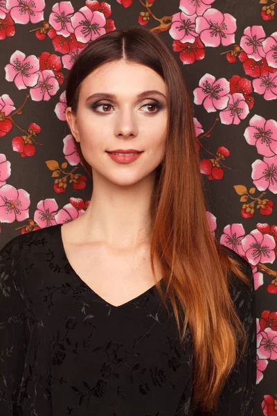 Портрет красивой женщины в черном платье. Фон из ткани в рисунке цветов — стоковое фото