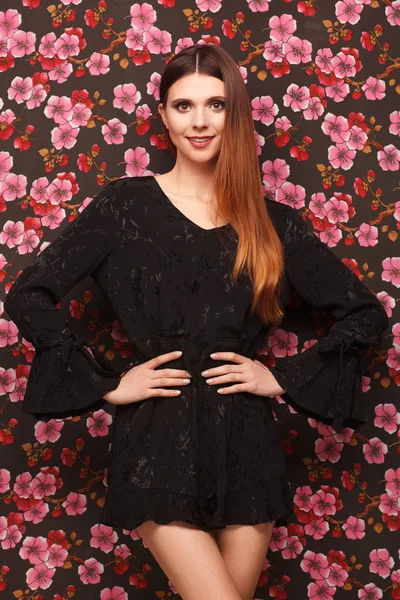 Портрет красивой женщины в черном платье. Фон из ткани в рисунке цветов — стоковое фото