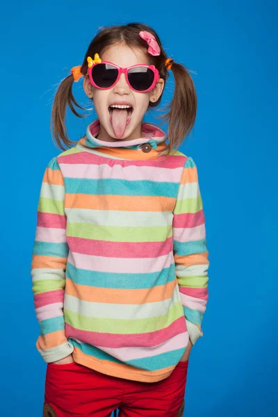 Retrato de uma menina emocional de cinco anos de idade em uma camisola listrada e em óculos infantis em um fundo azul — Fotografia de Stock