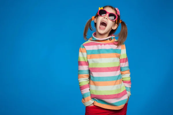 Retrato de uma menina emocional de cinco anos de idade em uma camisola listrada e em óculos infantis em um fundo azul — Fotografia de Stock