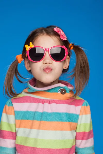 Retrato de uma menina emocional de cinco anos de idade em uma camisola listrada e em óculos infantis em um fundo azul — Fotografia de Stock
