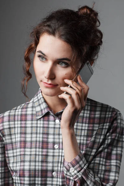 Портрет интеллигентной студентки с вьющимися волосами и телефоном в руке. Шахматная рубашка — стоковое фото