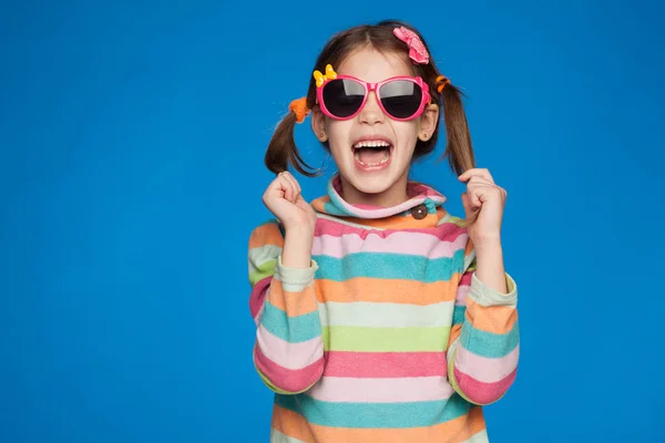 Retrato de uma menina emocional de cinco anos de idade em uma camisola listrada e em óculos infantis em um fundo azul — Fotografia de Stock