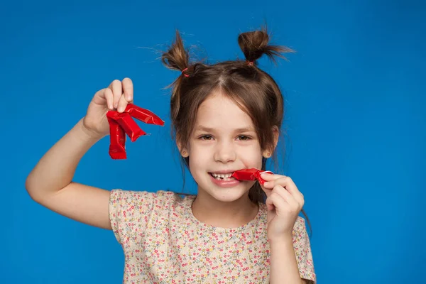 Retrato de uma menina bonita de cinco anos com um penteado interessante e com doces em suas mãos em um fundo azul — Fotografia de Stock