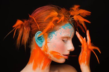 Turuncu tüyleri kullanarak yaratıcı makyaj ve saç modeli ile güzel bir model portresi