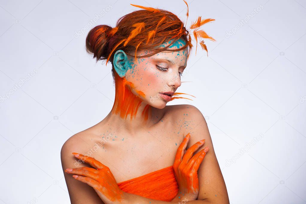 Portrait of a beautiful model with creative make-up and hairstyle using orange feathers