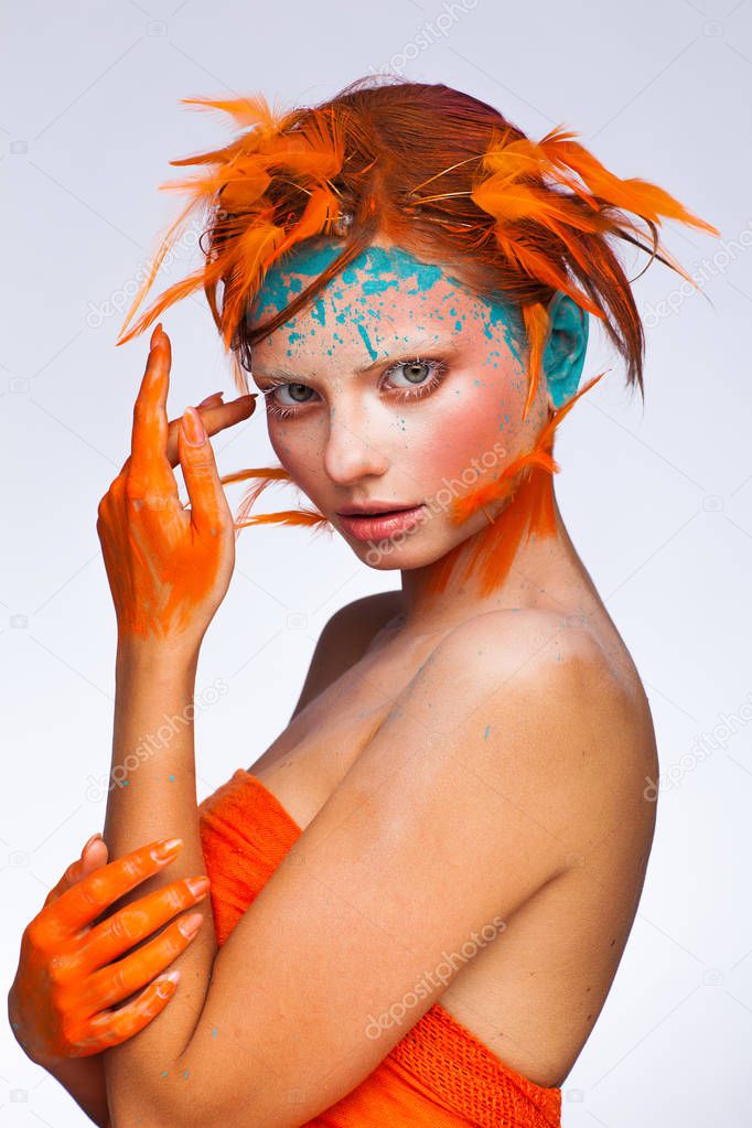 Portrait of a beautiful model with creative make-up and hairstyle using orange feathers