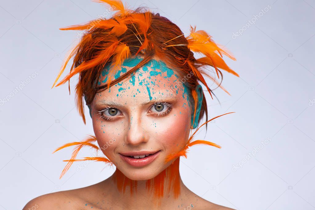 Portrait of a beautiful model with creative make-up and hairstyle using orange feathers