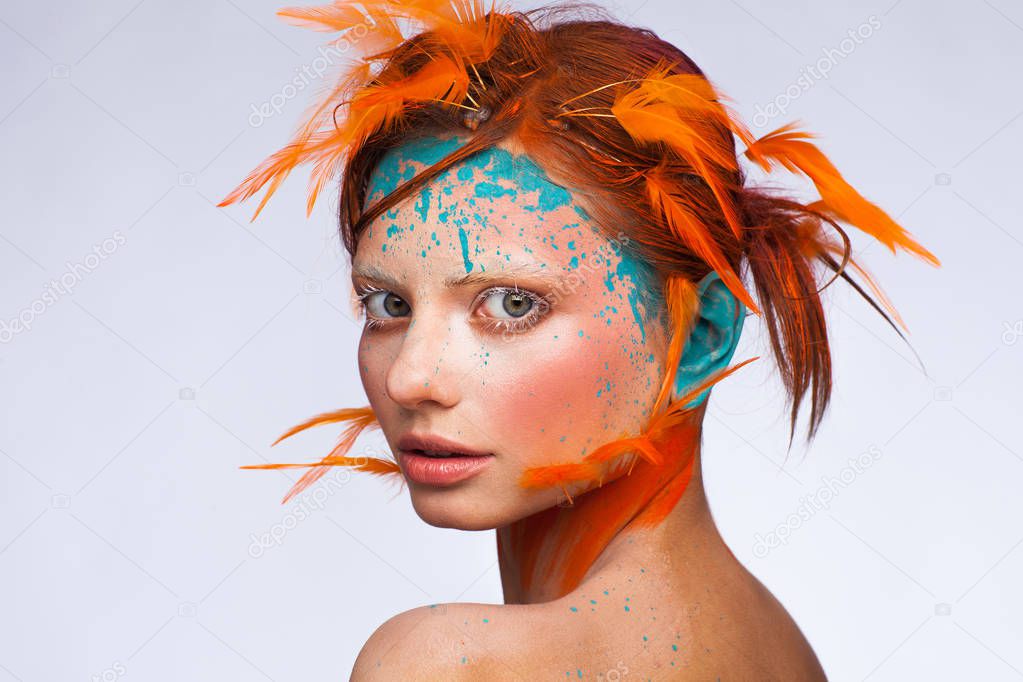 Portrait of a beautiful model with creative make-up and hairstyle using orange feathers