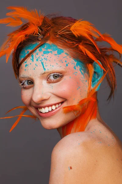オレンジ色の羽を使用した創造的なメイクアップとヘアスタイルの美しいモデルの肖像画 — ストック写真