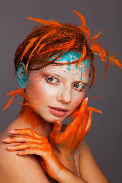 Portrait of a beautiful model with creative make-up and hairstyle using orange feathers — Stock Photo, Image