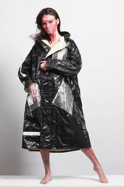 Model in a black raincoat made of cellophane and in creative make-up