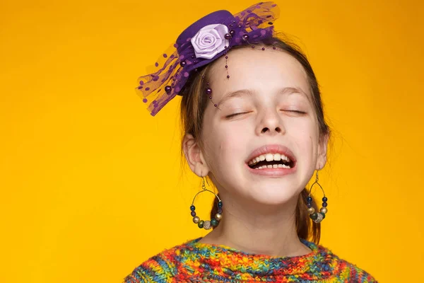 Retrato de uma menina alegre de 8 anos em um chapéu em miniatura e em uma camisola multicolorida. Fundo amarelo — Fotografia de Stock