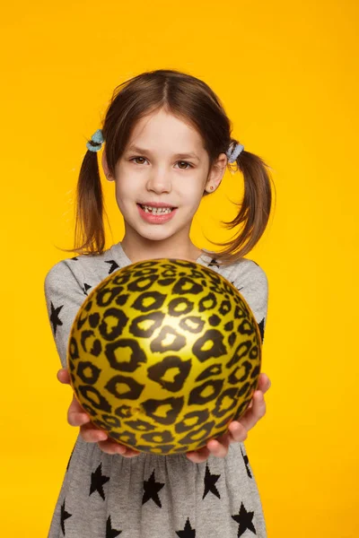 Portrait of a cheerful 5-year-old girl in a gray dress with drawings of stars and with an inflatable ball in her hands