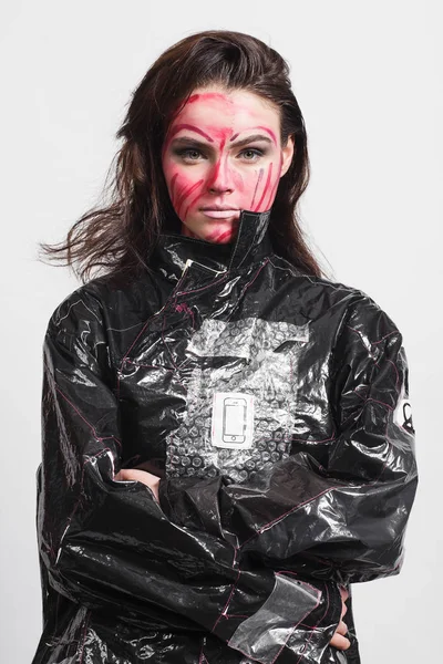 Model in a black raincoat made of cellophane and in creative make-up