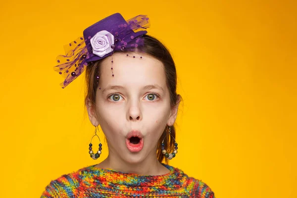 Retrato de uma menina alegre de 8 anos em um chapéu em miniatura e em uma camisola multicolorida. Fundo amarelo — Fotografia de Stock