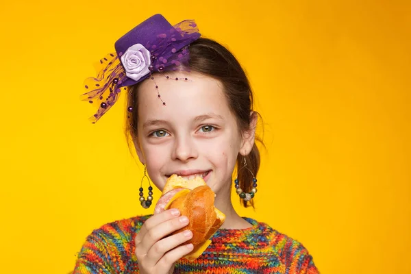 Porträt eines fröhlichen 8-jährigen Mädchens mit Miniaturmütze, buntem Pullover und einem Sandwich in der Hand — Stockfoto