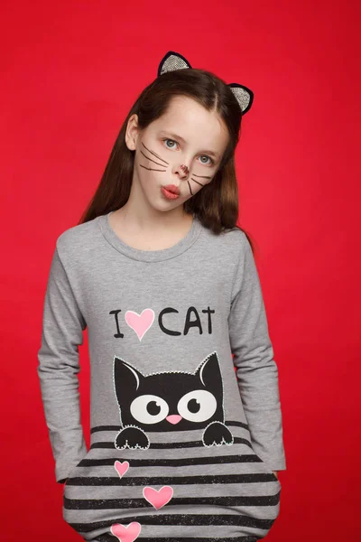 Kedi deseni ve kedi makyajı olan bir elbise içinde 8 yaşındaki neşeli bir kızın portresi. Kırmızı arka plan