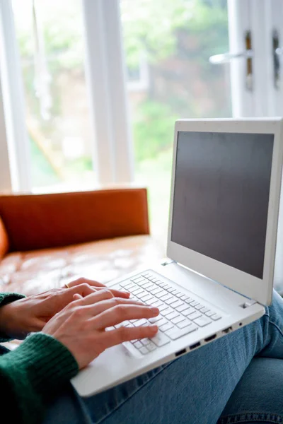 Femme à la maison en utilisant un ordinateur portable tout en se relaxant sur le canapé — Photo