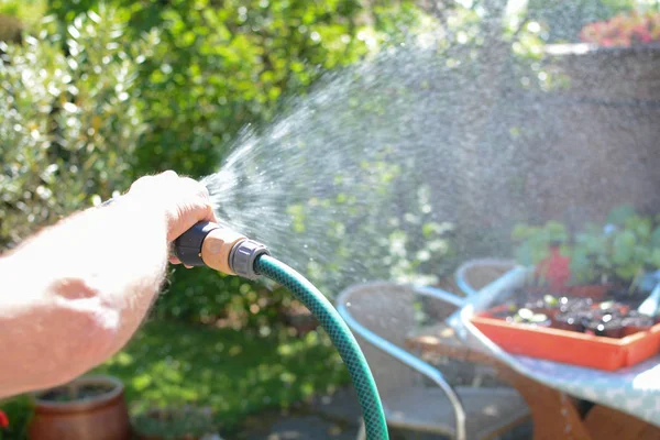 Homme arrosant le jardin avec un tuyau d'arrosage par une journée ensoleillée — Photo