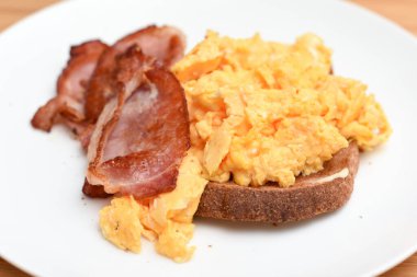 Pastırma ve çırpılmış yumurta ve beyaz tabakta bir dilim kızarmış ekmek.