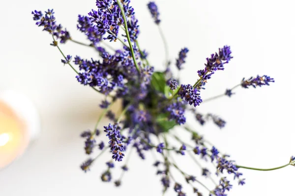 Scented candle and lavender flowers on white coffee table in home interior