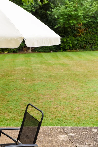 Patio garden umbrella and chair by the lawn of a home garden