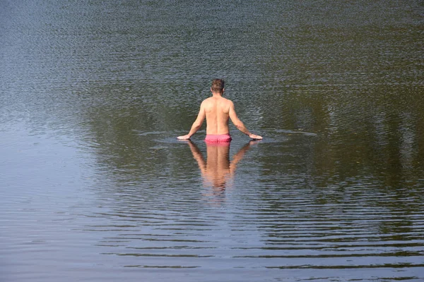 男は穏やかな水に反射して泳ぐために湖に出て行きます — ストック写真