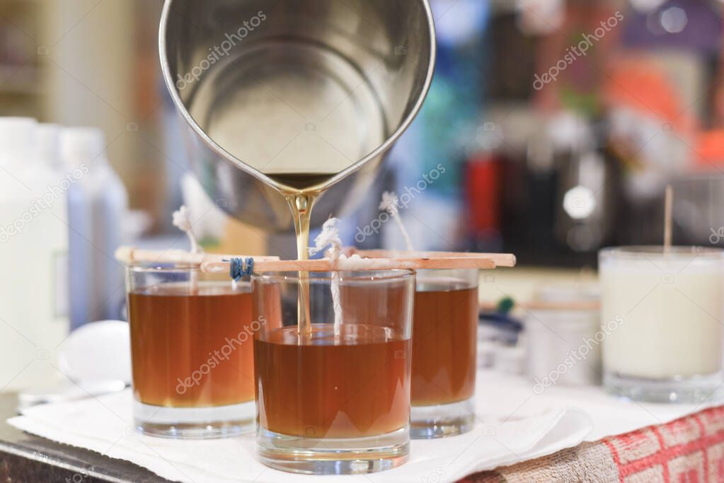 Creative occupation of candle making showing the pouring of liquid wax into jars