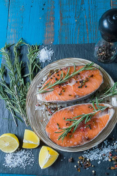 Raw fresh salmon fish before cooking , with lemon and spices, on a plate, over old blue wooden background, vertical.