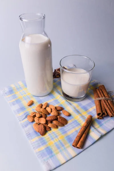 Front view. Natural milk in bottles and almond nuts and cinnamon sticks on white and blue napkin background.