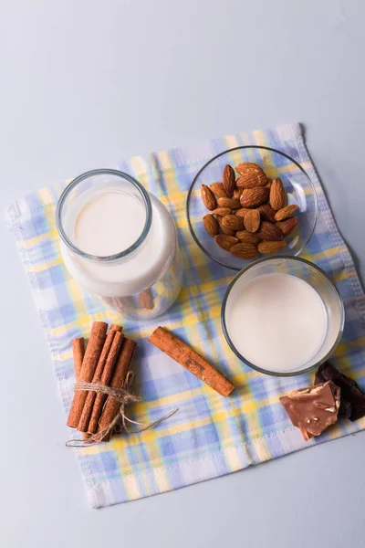 Front view. Natural milk in bottles and almond nuts and cinnamon sticks on white and blue napkin background, vertical.