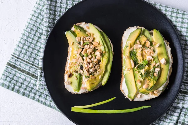 Avocado sandwiches with nuts and cream cheese on a plate, over napkin background. Healthy food for lunch or breakfast. Copy space, flat lay.