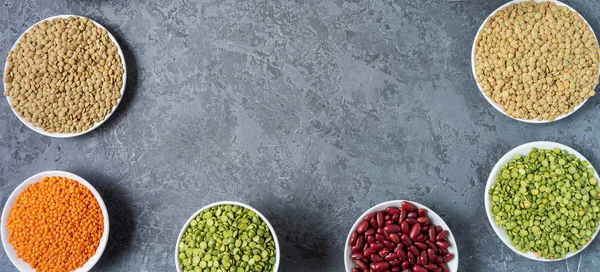 Top view of assortment of peas, lentils, beans and legumes over gray background.