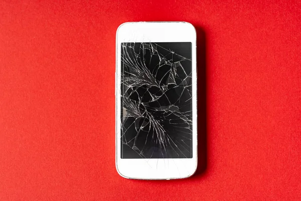Broken mobile phone with cracked display on red background.
