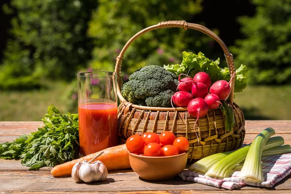 Fresh vegetables in a basket and tomato juice over green nature background.